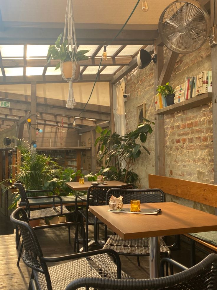 tables and chairs in a restaurant with plants hanging from the ceiling