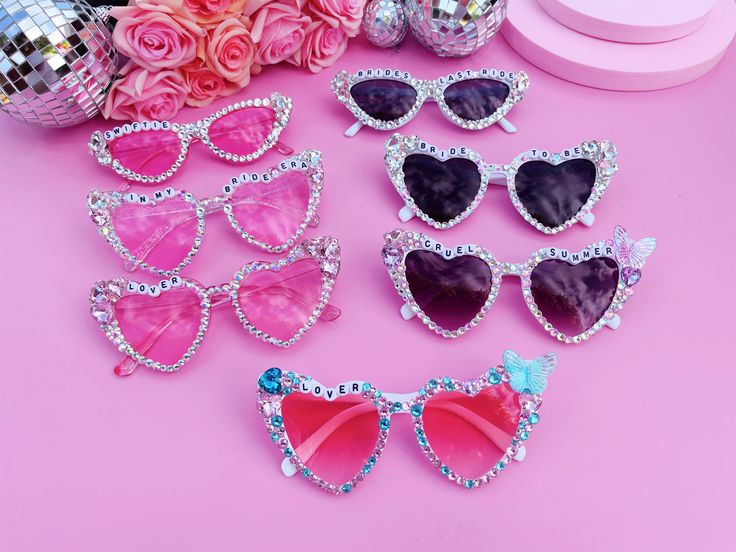 several pairs of heart shaped sunglasses sitting on top of a pink table next to flowers