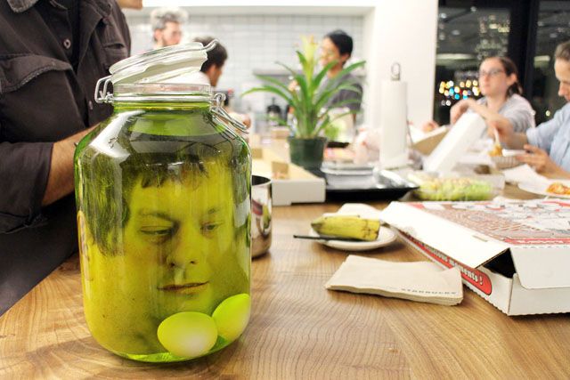 a jar filled with pickles sitting on top of a wooden table next to other people