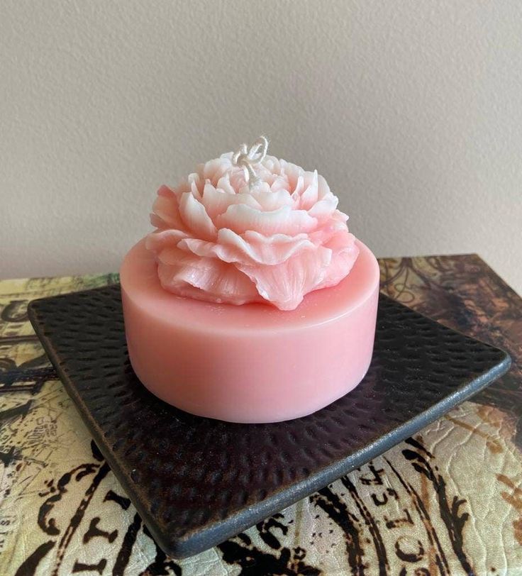 a pink soap with white flowers on top sits on a black plate next to a wall