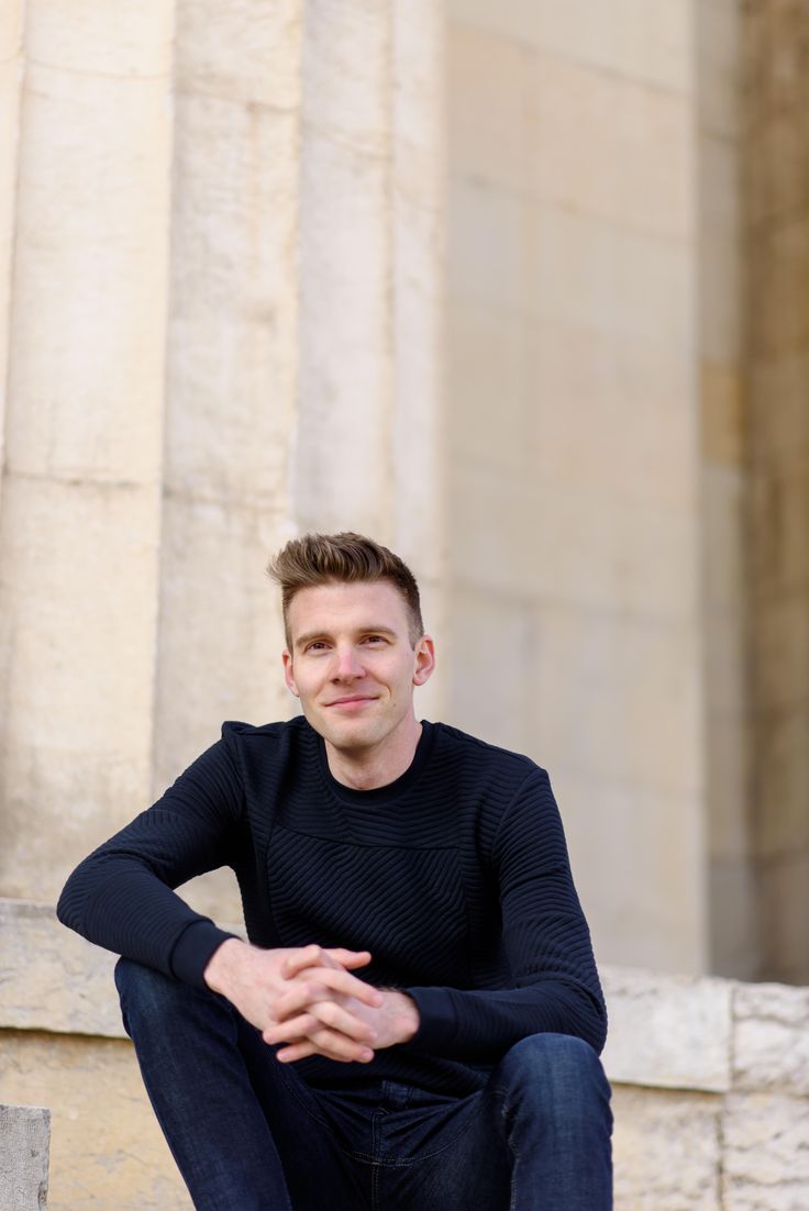 a man is sitting on the steps in front of some pillars and posing for a photo