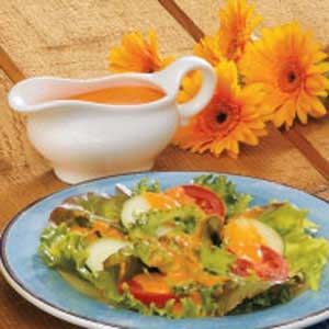 a blue plate topped with salad next to a white bowl filled with dressing and flowers