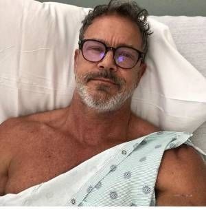 a man with glasses laying in a hospital bed