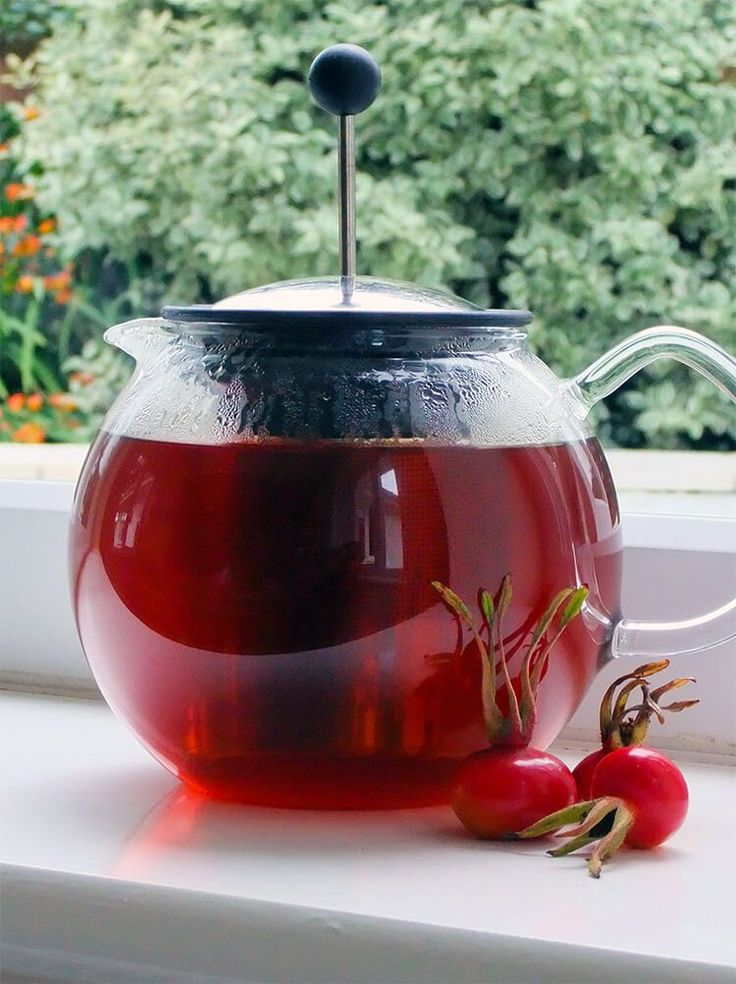 a tea pot filled with red liquid next to two cherries on a window sill