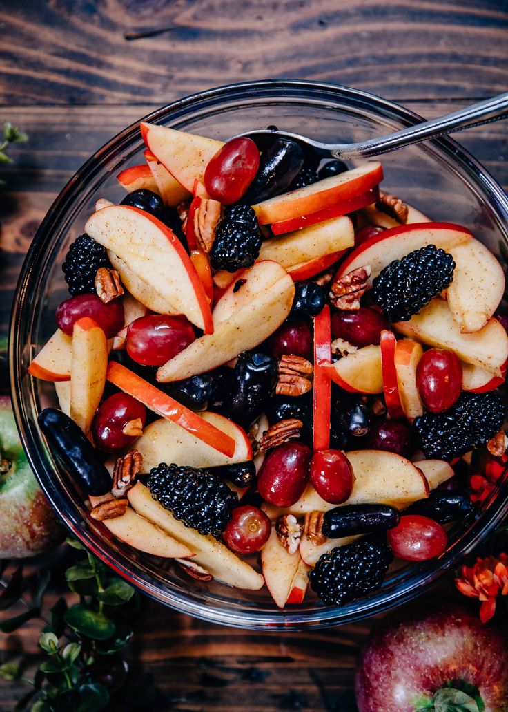 a glass bowl filled with fruit and nuts on top of a wooden table next to an apple