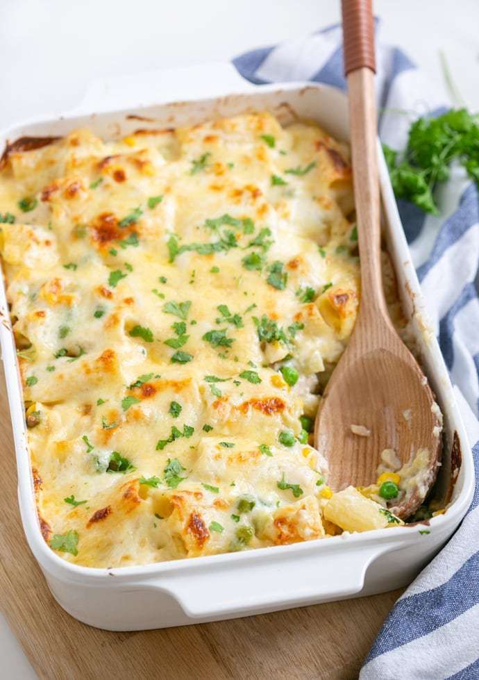 a casserole dish with cheese and vegetables in it on a wooden cutting board