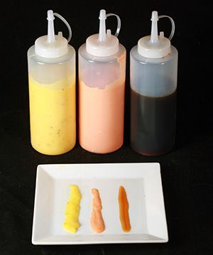 three bottles with different colored liquids on them next to a white plate and black background