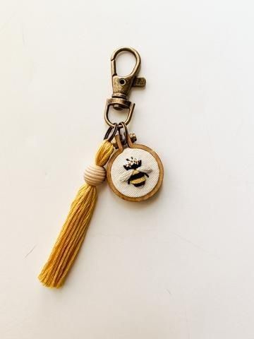 a yellow tasseled keychain with a small embroidered bee on it's side