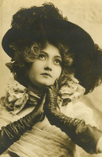 a black and white photo of a woman wearing a hat with gloves on her hands