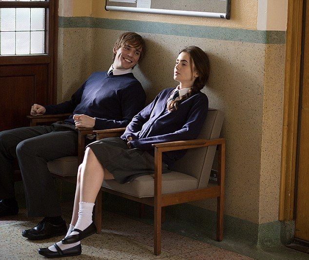 a man and woman sitting on a chair in front of a wall with a clock