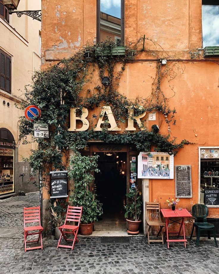 the outside of a bar with tables and chairs in front of an orange building that has ivy growing on it