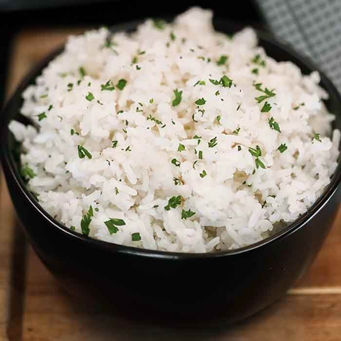 a black bowl filled with white rice and garnished with parsley on top