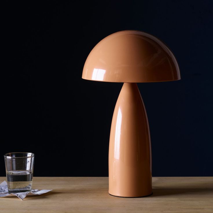 an orange lamp sitting on top of a wooden table next to a glass filled with water