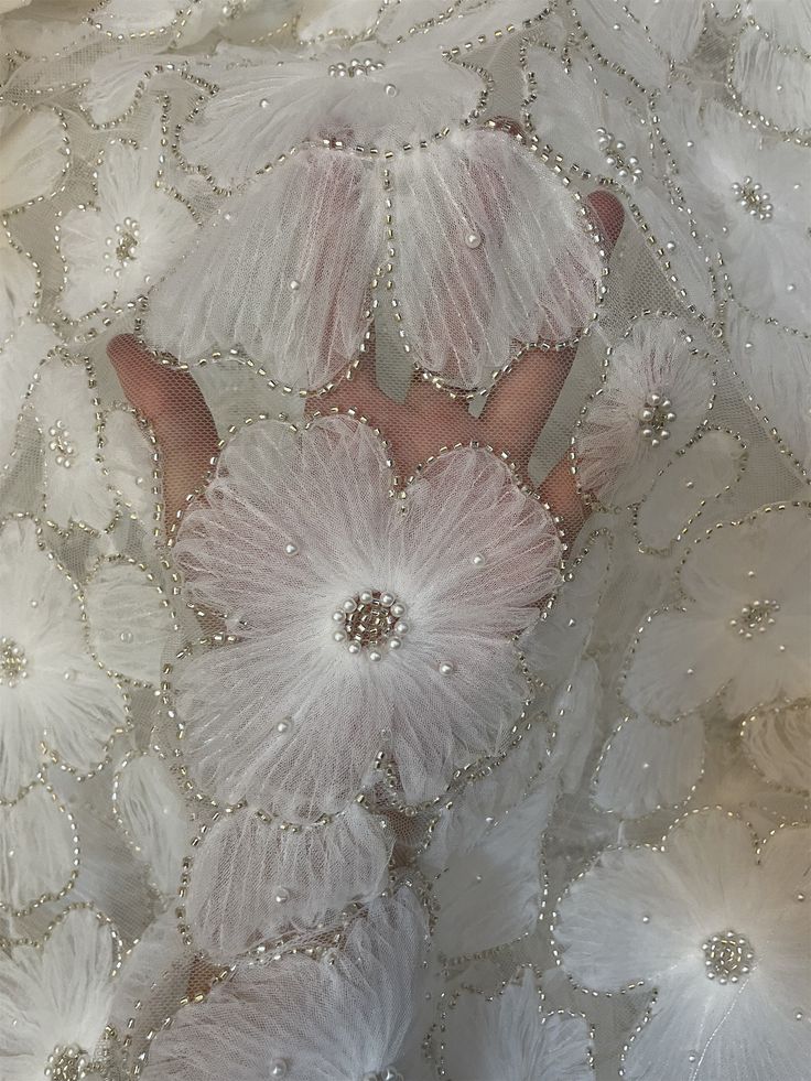 a close up of a person's hand in a white dress with flowers on it