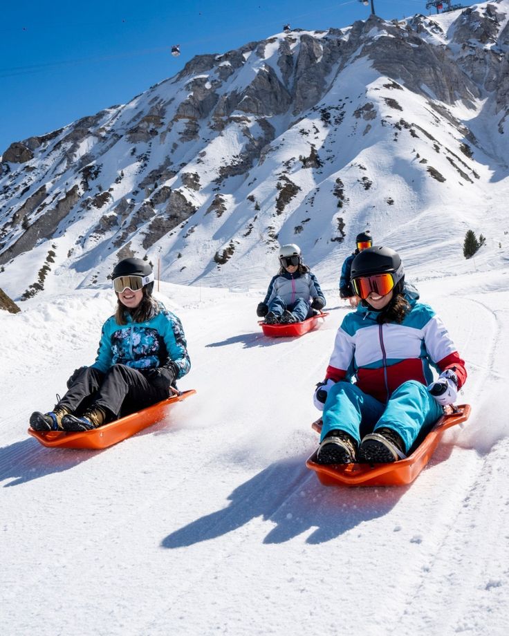 three children are sledding down a snowy hill on their snowboards and skis