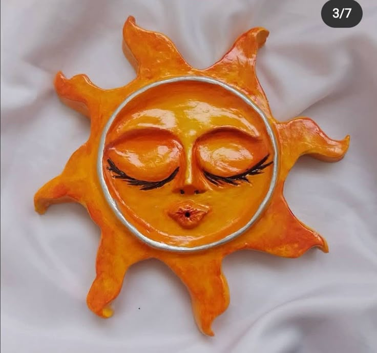 an orange sun with eyes and eyelashes on it's face is shown in front of a white sheet