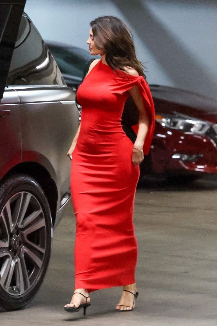 a woman in a red dress walking towards a car