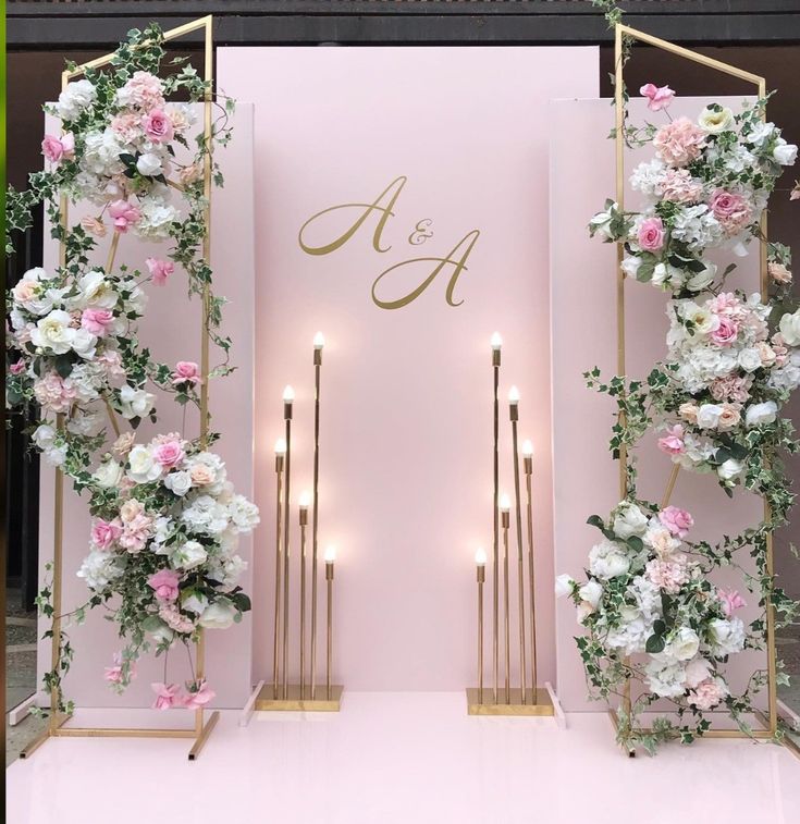 a pink and gold wedding arch with flowers on the front, candles in the back