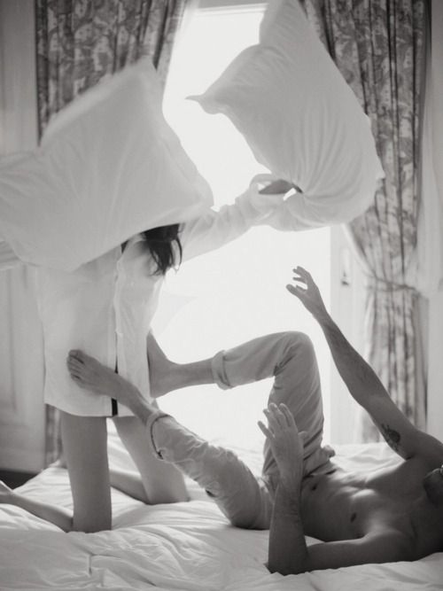 two women laying on top of a bed with pillows over their heads and one woman reaching for the pillow