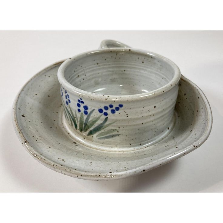 a white bowl with blue flowers on it and a saucer in the shape of a cup