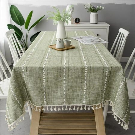 a table with a green tablecloth and white chairs in front of a potted plant