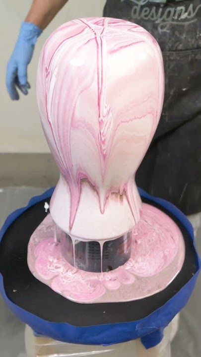 a person in blue gloves is painting a pink vase with white and black swirls