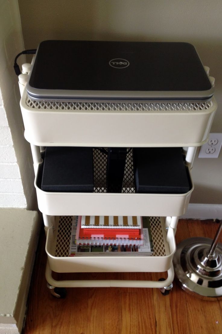 a laptop computer sitting on top of a white cart next to a lamp and wood floor