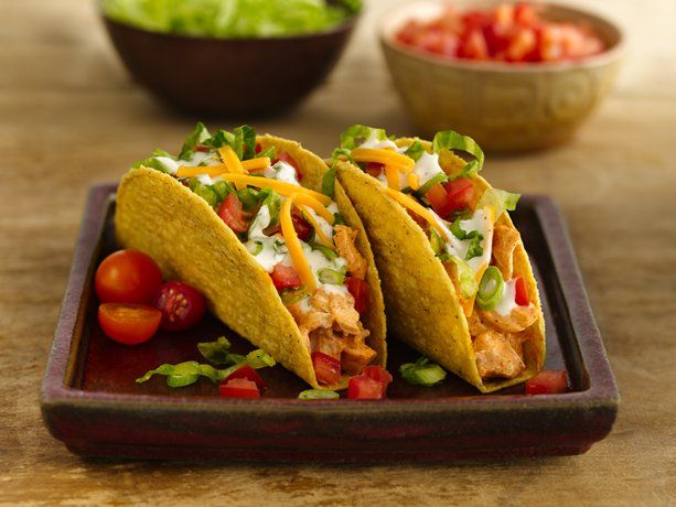 three tacos on a plate with tomatoes and lettuce in the bowl next to it