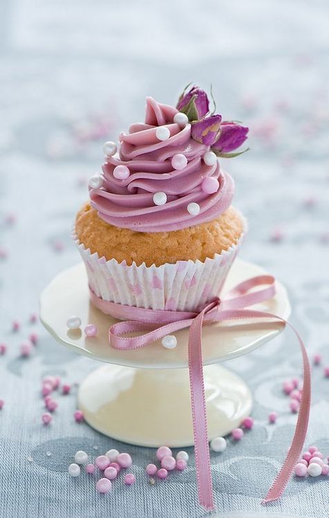 a cupcake with pink frosting and a flower on top sitting on a plate