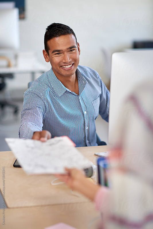 a man sitting at a desk in front of a computer smiling and talking to someone else