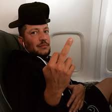 a man sitting on an airplane with his hand up in the air and pointing to the side