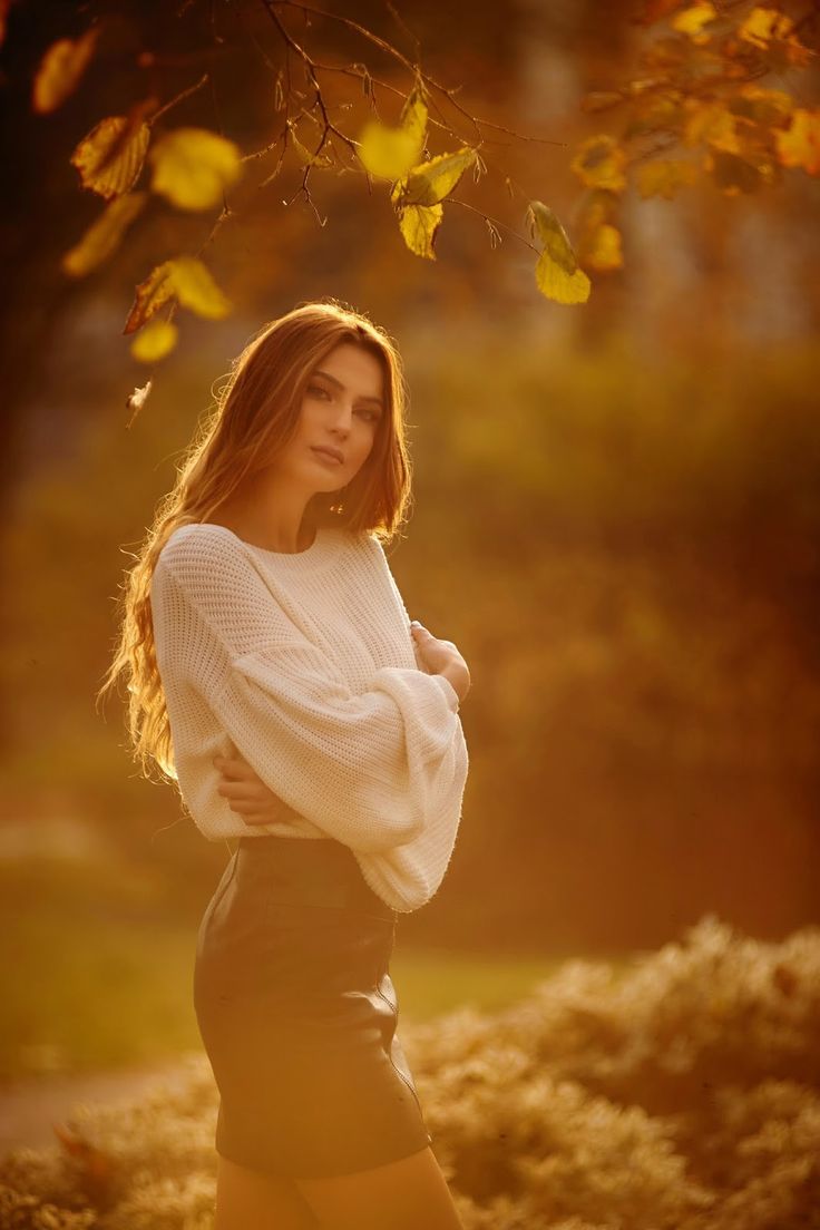 a beautiful young woman standing in front of a tree with her hands on her hips