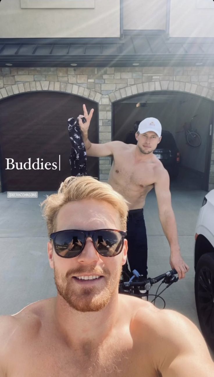 two shirtless men standing in front of a building with one holding up the peace sign