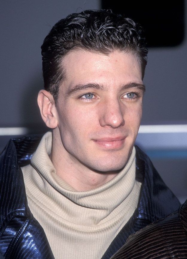 a close up of a person wearing a jacket and turtle neck sweater, looking at the camera