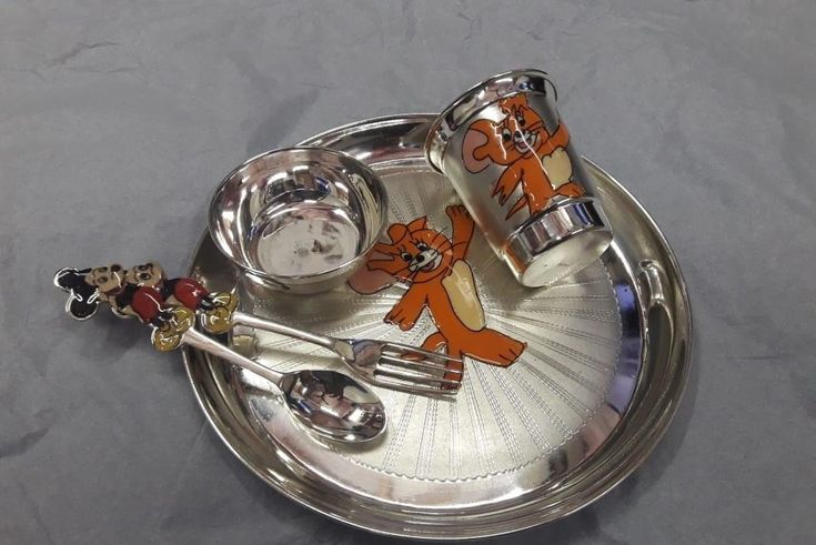 a silver tray with two spoons and a clock on it