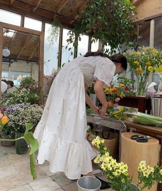 a woman in a white dress is cutting up some flowers at a table with pots and pans