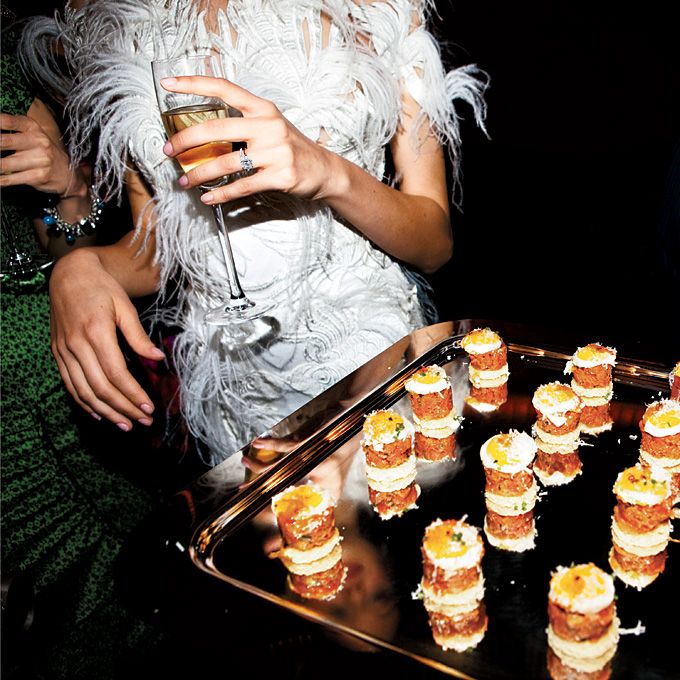 a woman is holding a glass in her hand and looking at some food on a tray