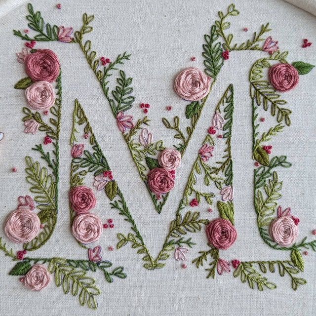 the letter m is made up of pink flowers and green leaves on a white background