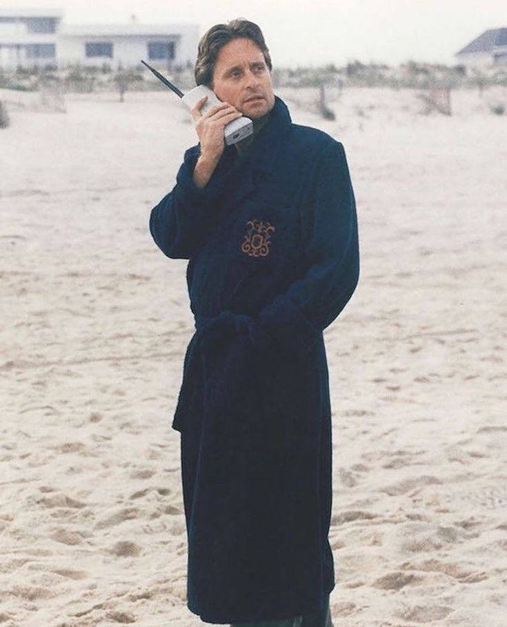 a man standing on the beach talking on his cell phone while wearing a bathrobe