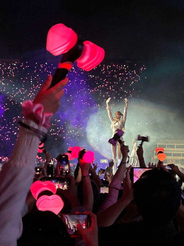 the crowd is holding up their cell phones to take pictures with fireworks in the background