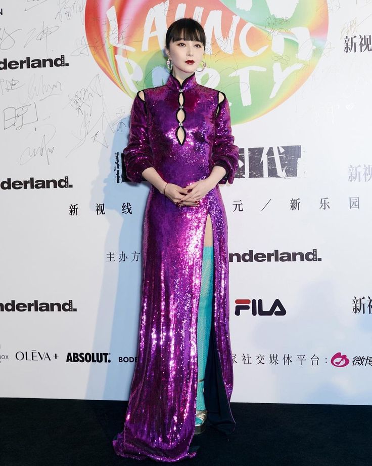 a woman in a purple dress standing on a black carpet