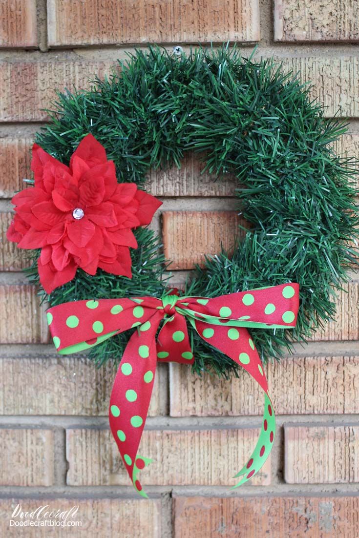 a green wreath with red poinsettia and polka dot ribbon on a brick wall