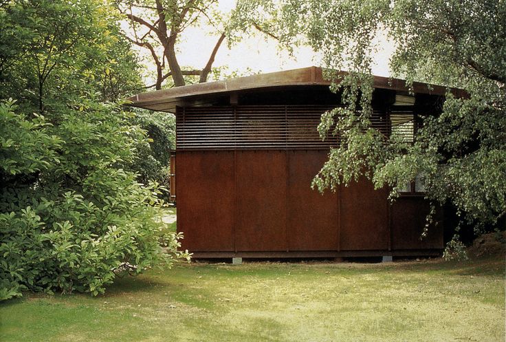 a small wooden structure sitting in the middle of a lush green field next to trees