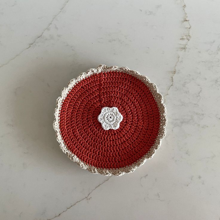 a red and white crocheted basket sitting on top of a marble counter