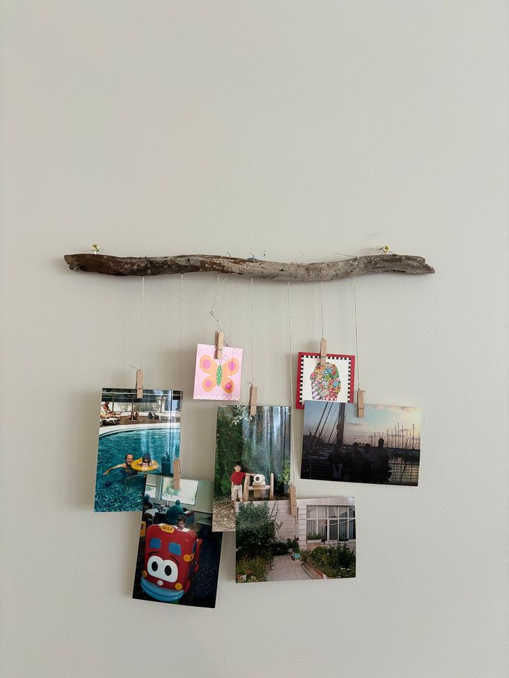 some pictures hanging on a white wall with a wooden stick attached to the wall next to them