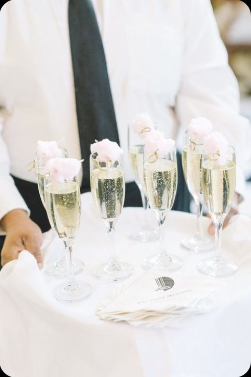 the waiter is holding four champagne flutes with pink flowers on them and napkins in front of him