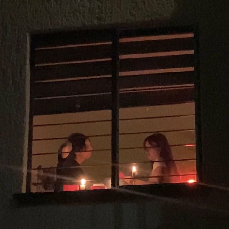 two people sitting at a table with candles in front of them, looking out the window