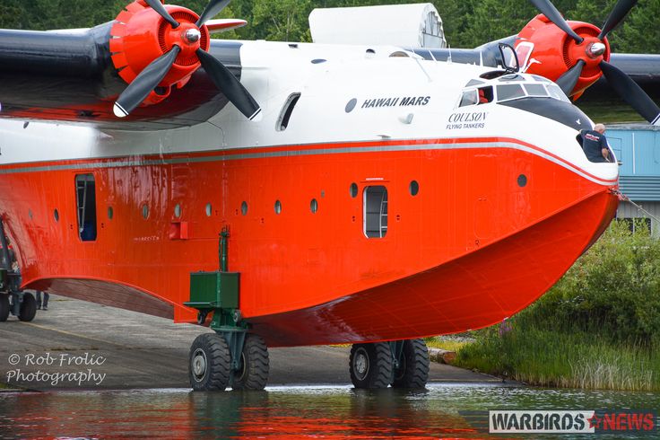 an orange and white airplane parked on the tarmac next to some water with trees in the background