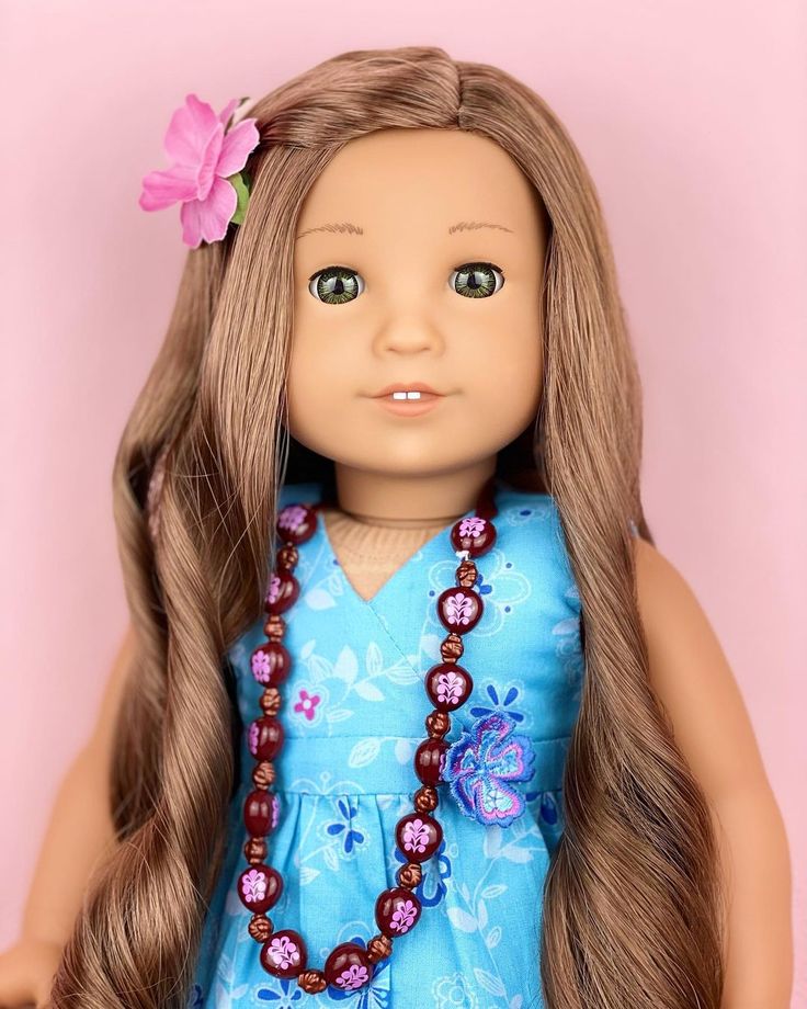 a close up of a doll with long blonde hair wearing a blue dress and pink flower in her hair