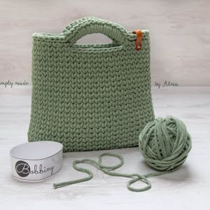 a green knitted bag next to a ball of yarn and a can of yarn